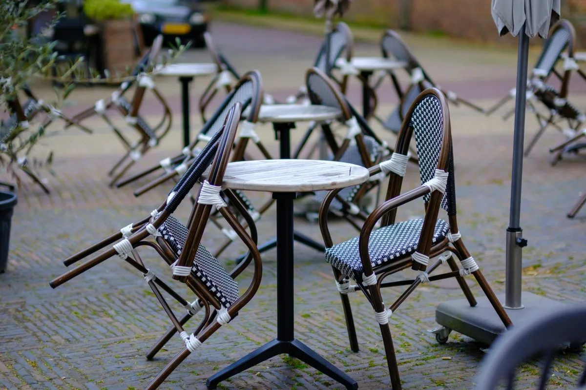 Empty patio tables and wicker chairs on a cobbled terrace in Amsterdam.